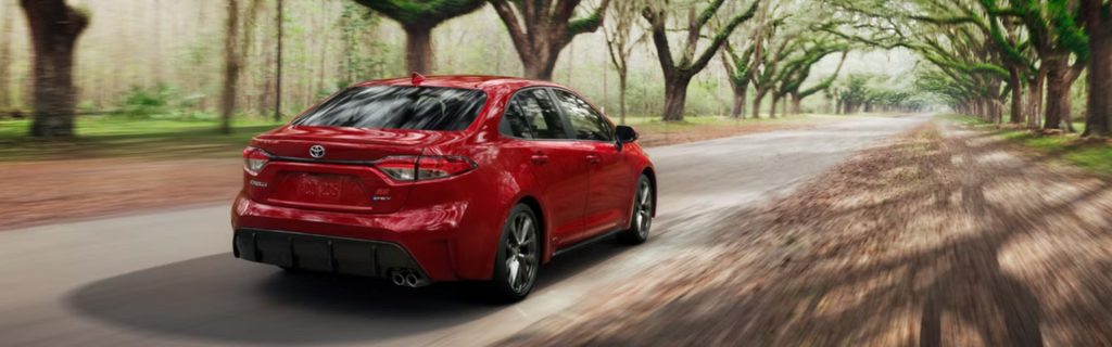 2026 Toyota Corolla driving along a tree-lined road, shown from the rear with motion blur highlighting smooth performance.