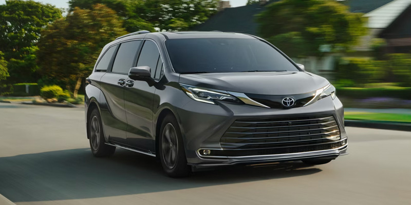 A 2026 Toyota Sienna driving along a road surrounded by greenery and trees.