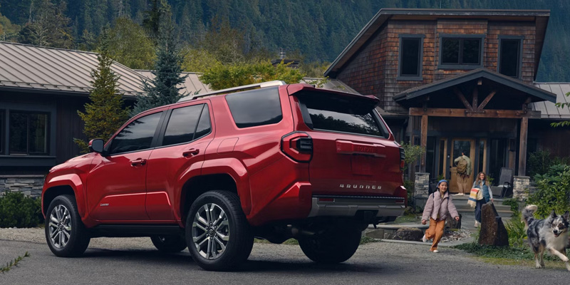 A red 2026 Toyota 4Runner is parked outside a cabin, with greenery and trees in the background.