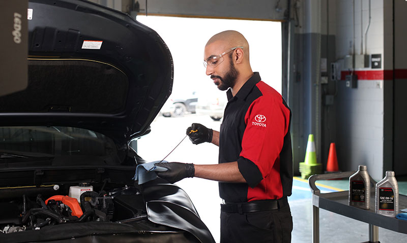 A professional in a red and black shirt is repairing a car, focused on the engine with tools in hand.
