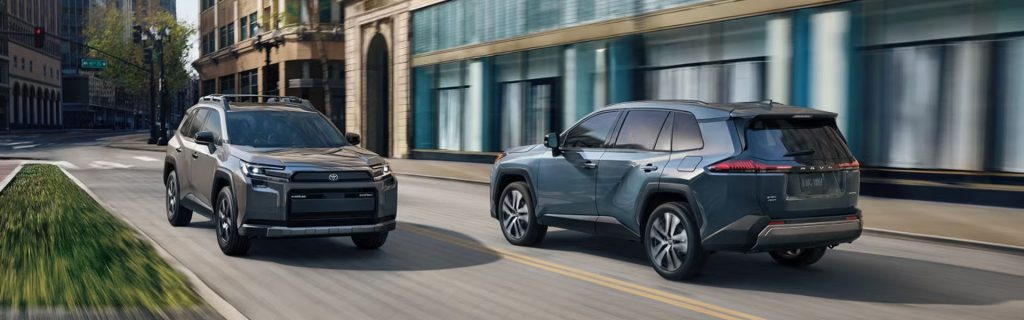 Two Toyota SUVs driving on a city street with buildings in the background.