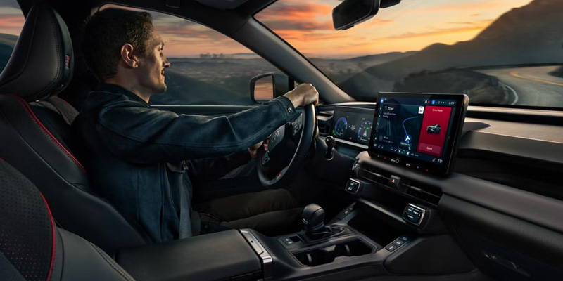 A person driving a Toyota car with a scenic view outside, featuring a digital dashboard display.
