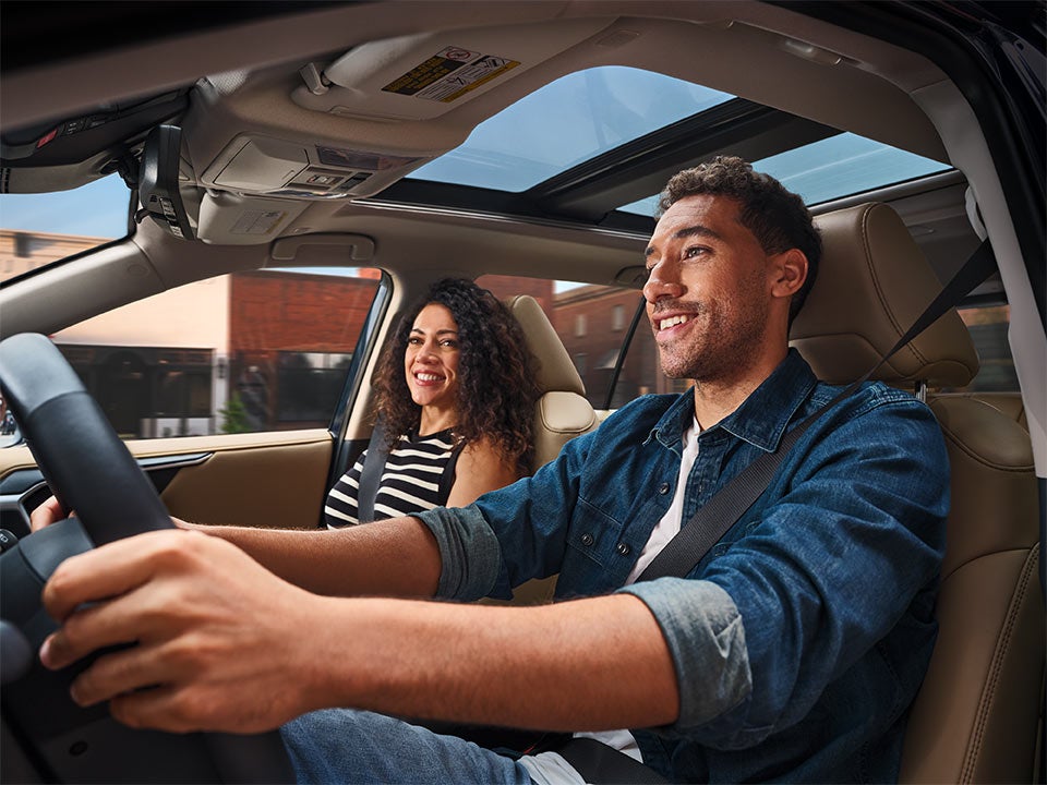 A happy young man driving a car with a young woman passenger, both smiling.