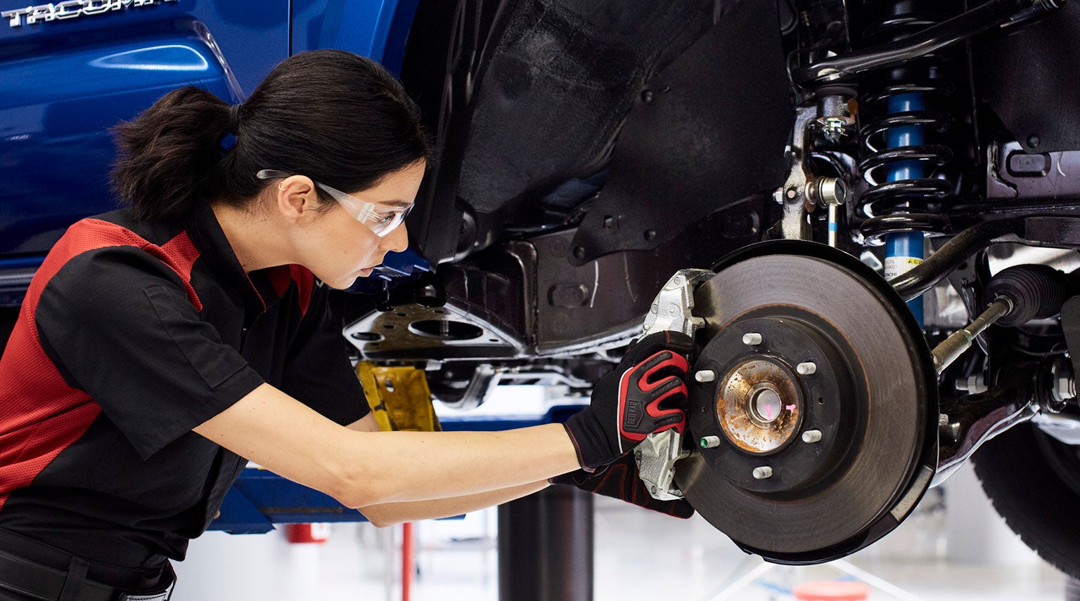 A person working on the brake system of a car, wearing protective eyewear and gloves.