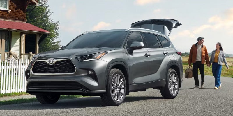A gray Toyota Highlander parked on a road, with two people walking beside it.