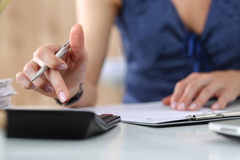 A person holding paper and pen in hand using calculator