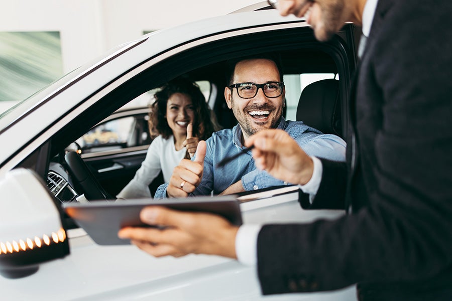 A customer who seats inside the car shows thumbs up to salesperson